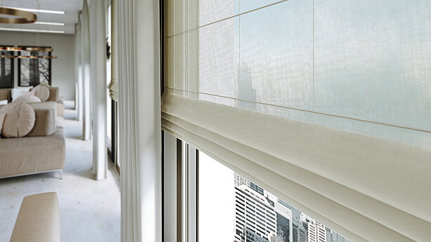 Elegante, halbtransparente Raffrollos und fliessende Vorhänge in einem modernen Wohnraum mit bodentiefen Fenstern und Stadtblick.