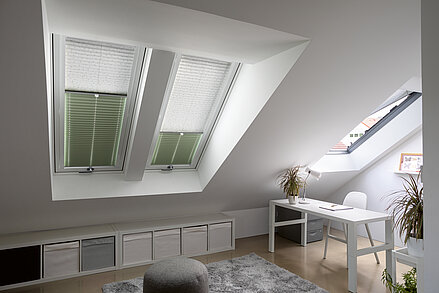 Zweifarbige Plissees in Weiss und Grün an Dachfenstern in einem hellen Arbeitszimmer im Dachgeschoss.