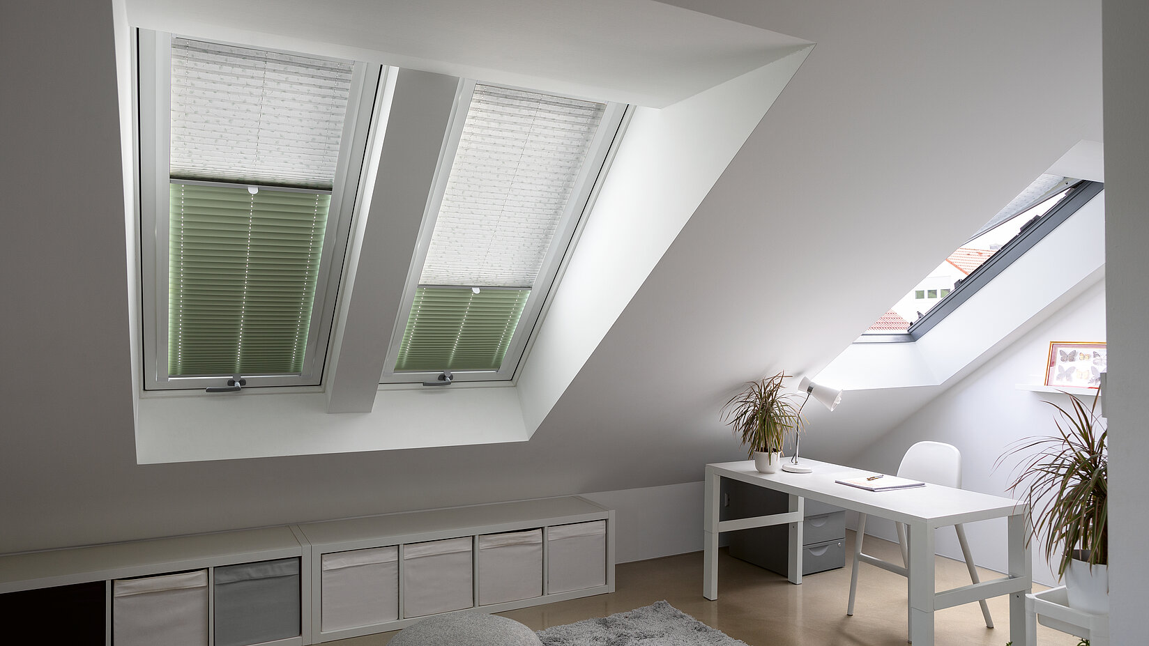 Zweifarbige Plissees in Weiss und Grün an Dachfenstern in einem hellen Arbeitszimmer im Dachgeschoss.