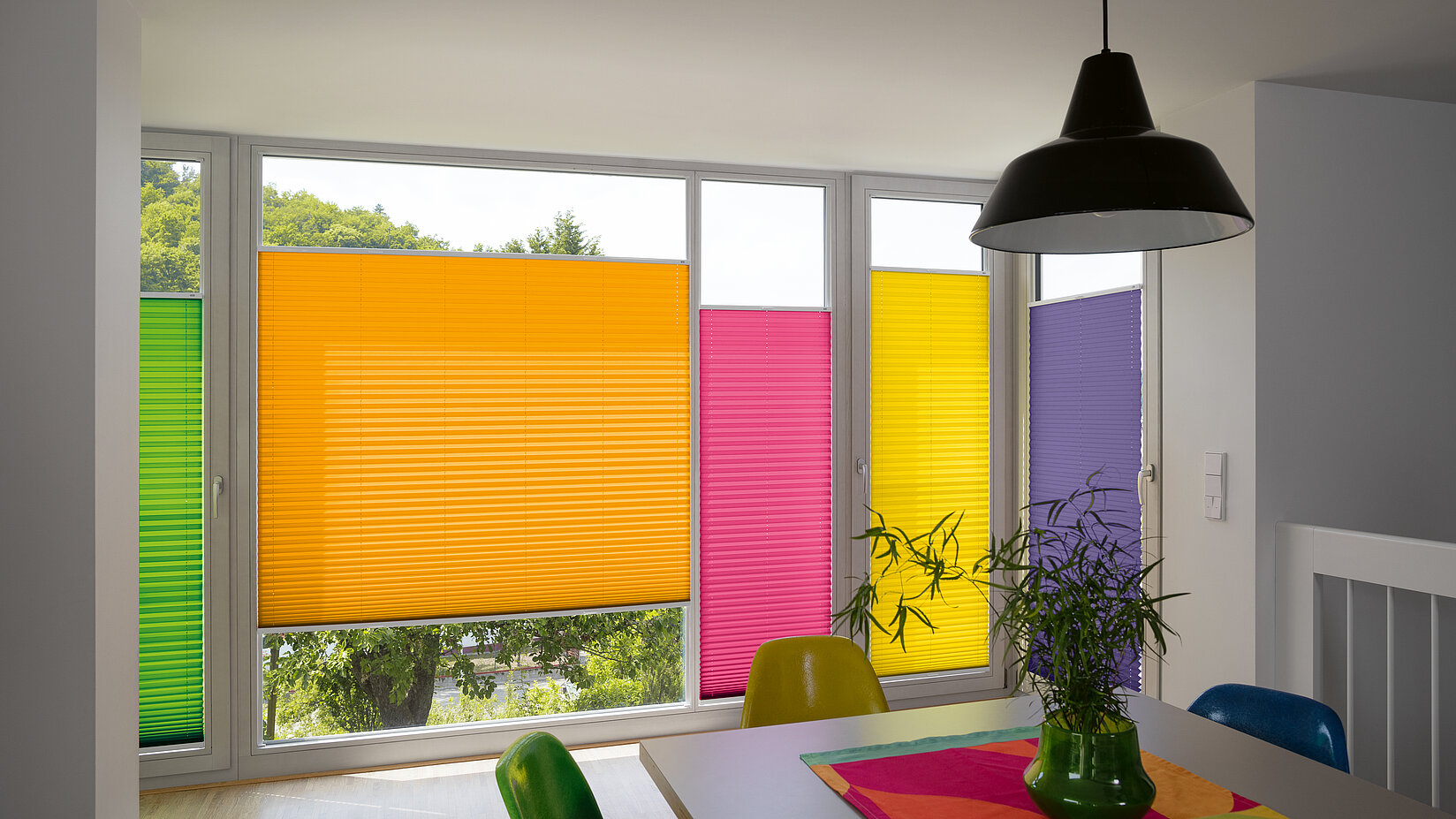 Bunte Plissees in RAL-Farben an bodentiefen Fenstern in modernem Essbereich mit farblich passender Einrichtung.