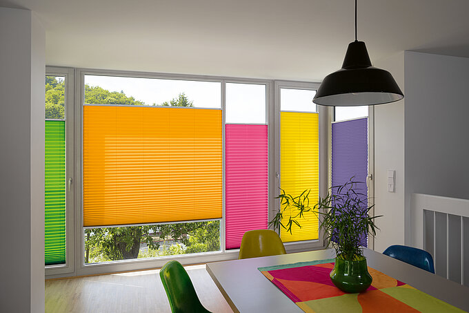 Bunte Plissees in RAL-Farben an bodentiefen Fenstern in modernem Essbereich mit farblich passender Einrichtung.