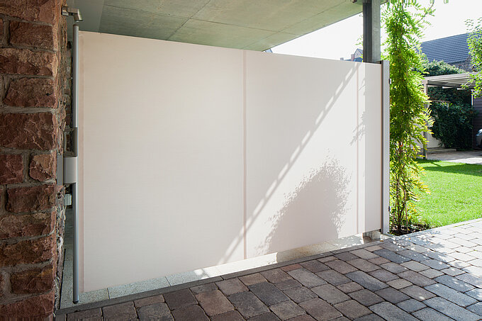 Cremefarbene Seitenmarkise als Sichtschutz auf einer Terrasse mit Blick in einen Garten.