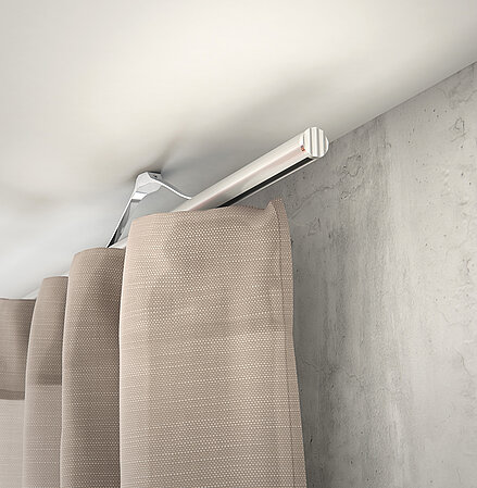 MHZ Vorhangstange „Novella“ in heller Aluminiumoptik, deckenmontiert mit beigefarbenen Stoffvorhängen vor Betonwand.