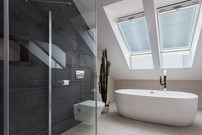 Badezimmer mit freistehender Wanne und Jalousien im Dachfenster. Lamellen verlaufen parallel zur Fensterfläche und filtern das Licht.
