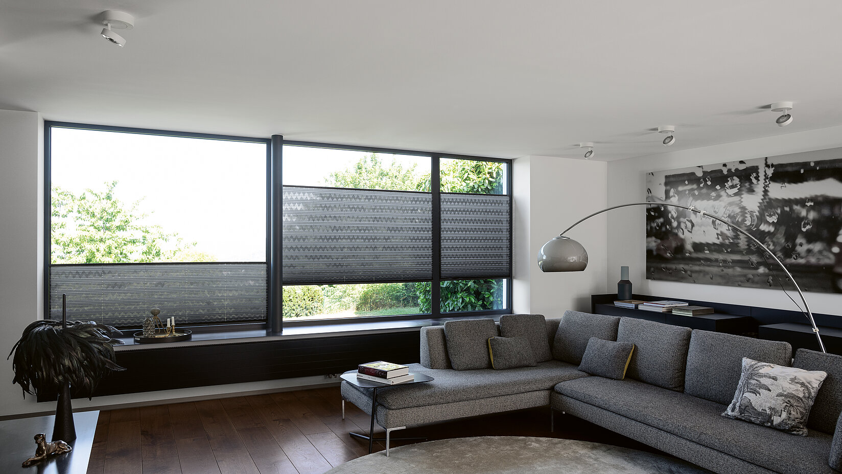 Dunkelgraue Plissees mit grafischem Muster in einem modern eingerichteten Wohnzimmer mit Ecksofa