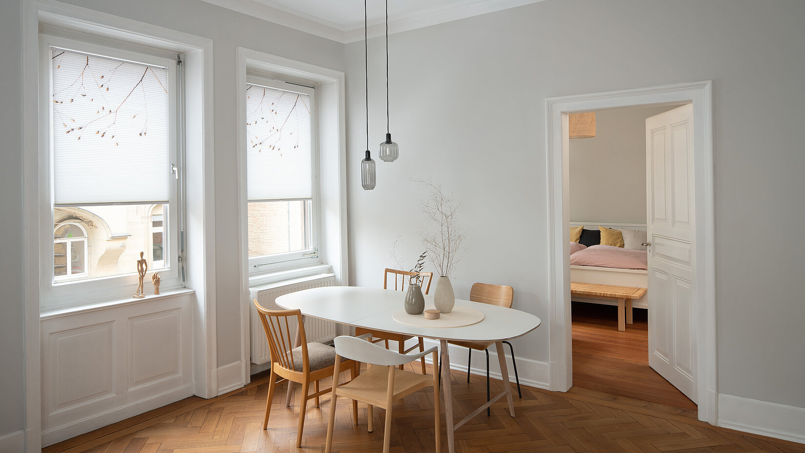 Zwei weiße Fenster mit floral bedruckten Wabenplissees in einem hellen Esszimmer mit Holzfußboden.