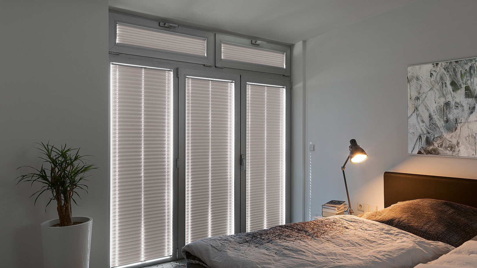 Lichtundurchlässige graue Plissees an bodentiefen Fenstern in einem modernen Schlafzimmer.