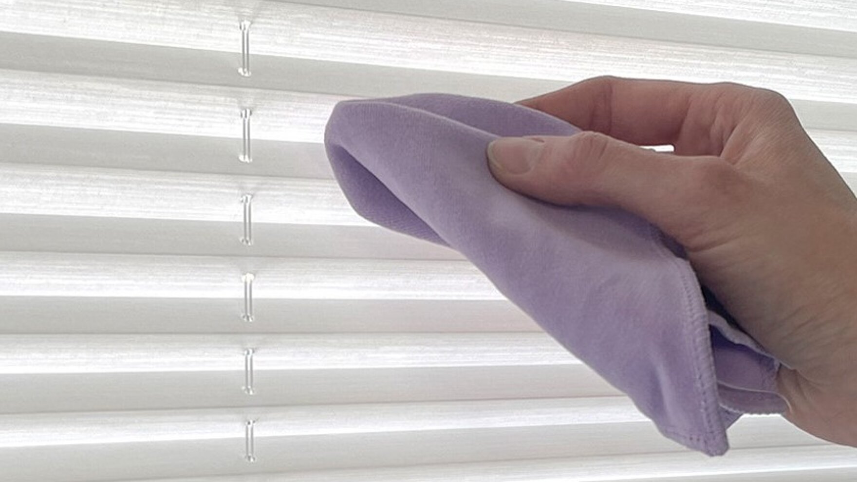 Hand wischt weisses Plissee mit einem violetten Mikrofasertuch ab.