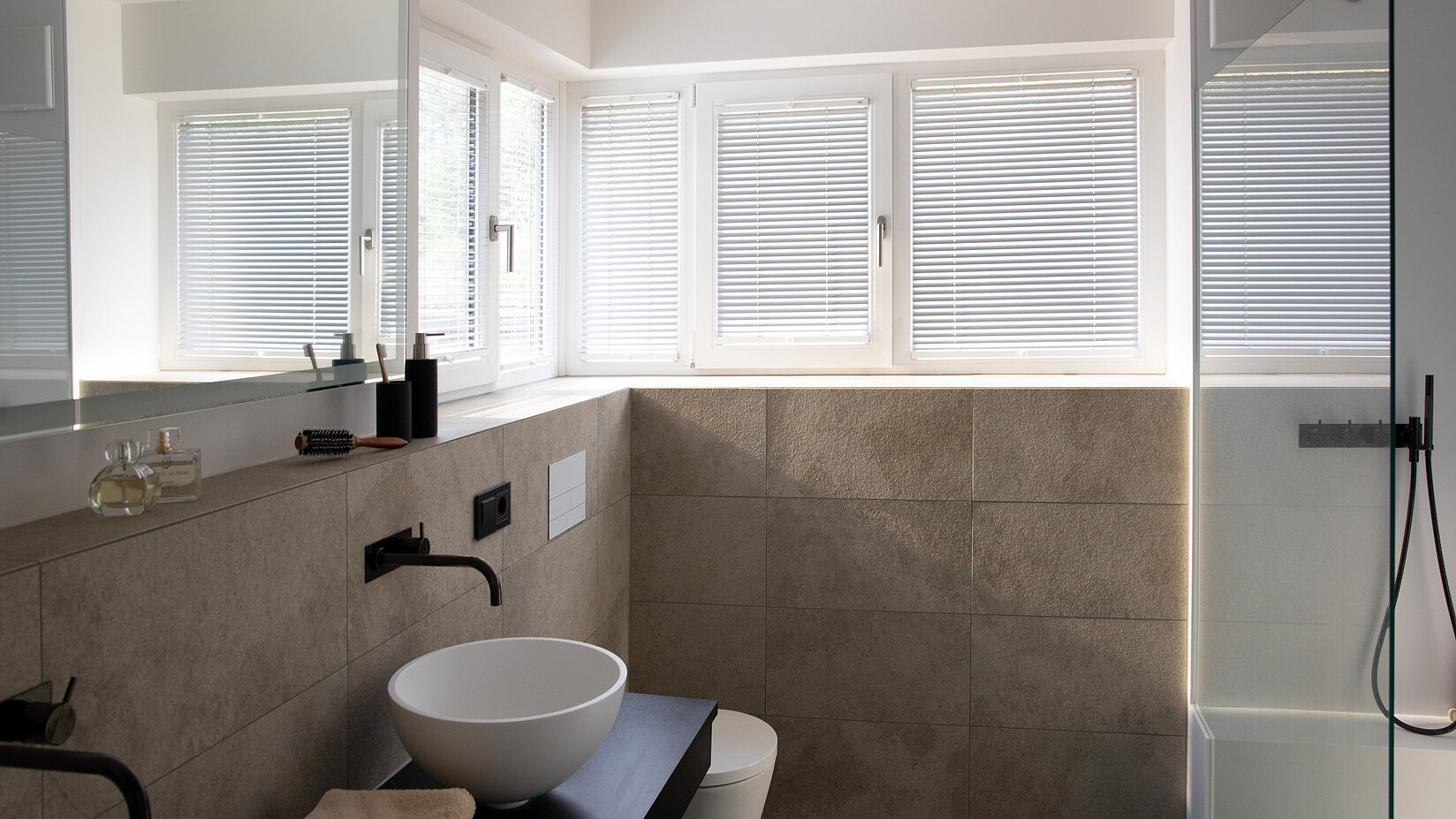 Badezimmer mit mehreren Fenstern und hellen Jalousien. Horizontale Lamellen bieten Sichtschutz und Lichtsteuerung.