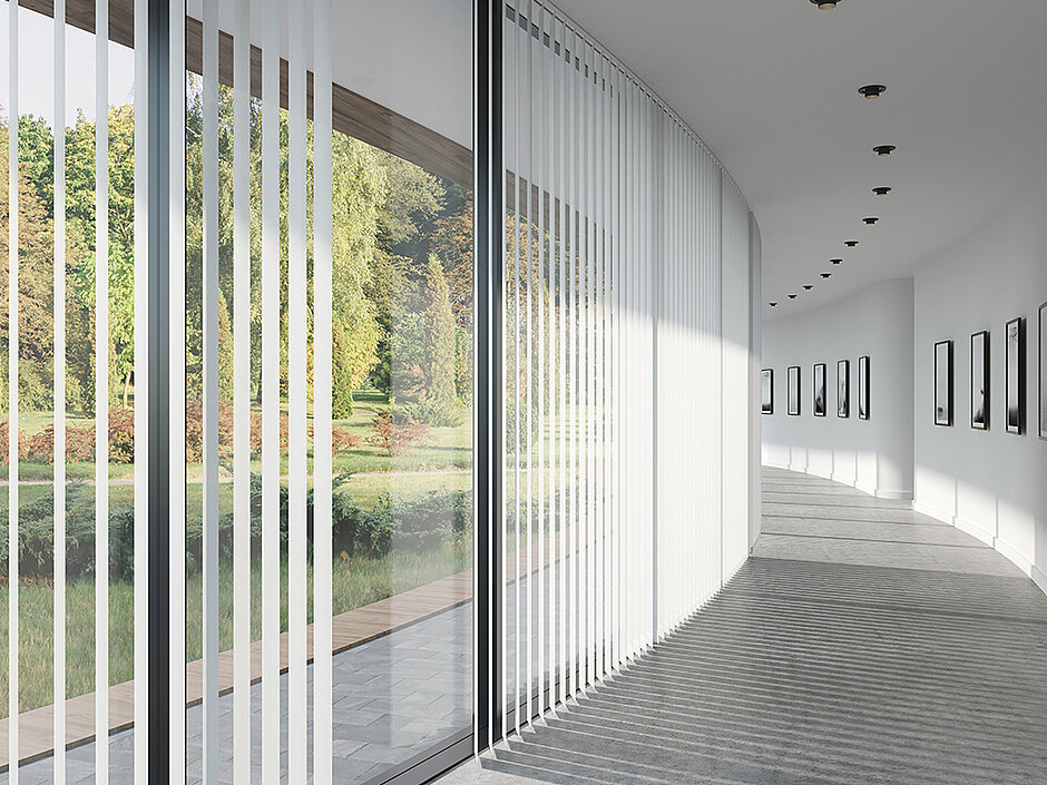 Innenraum mit geschwungenem Lamellenvorhang aus weißen vertikalen Lamellen vor bodentiefen Fenstern.