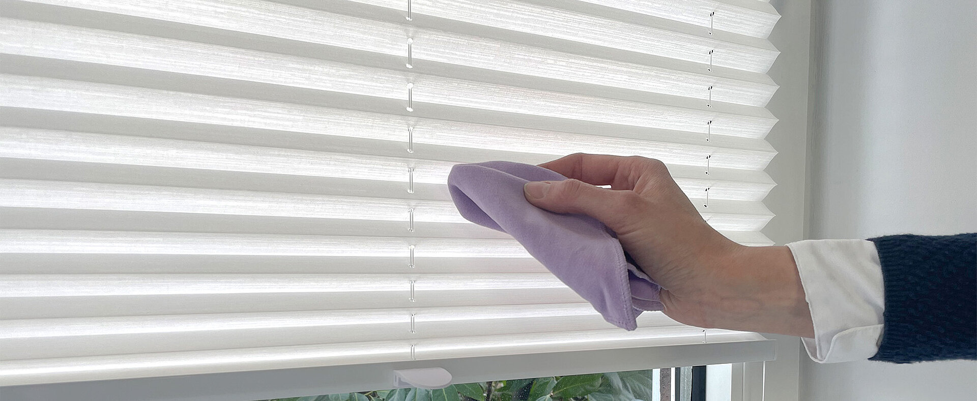 Hand wischt mit einem weichen Tuch über ein weisses Plissee zur Reinigung.