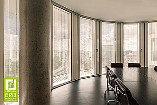 Ein moderner Besprechungsraum mit einem grossen Tisch und Stühlen. Die raumhohen Fenster sind mit vertikalen Metallbehängen ausgestattet, die den Raum vor Sonneneinstrahlung schützen.