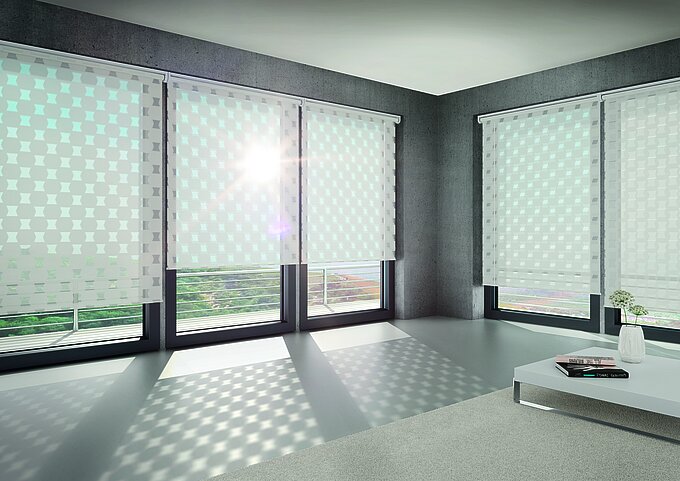 Modernes Wohnzimmer mit grossen Fenstern und dem MHZ Doppelrollo „Oscar“ mit grafischem Muster, das dekorative Lichtreflexe auf Boden und Wand wirft.