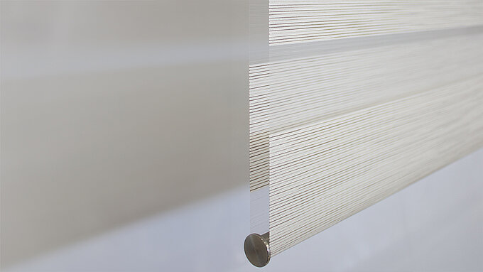 Nahaufnahme der Stoffkante eines weissen MHZ Doppelrollos mit feiner horizontaler Streifenstruktur und metallischem Abschlussprofil.