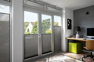Graue Plissees als Sicht- und Blendschutz in modernem Homeoffice mit Schreibtisch und Oberlichter