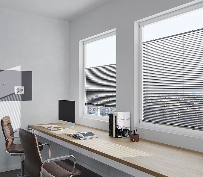 Büro mit zwei Fenstern und Jalousien. Horizontale Lamellen sorgen für blendfreies Arbeiten am Computer.