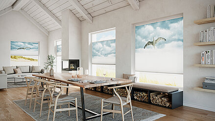 Modernes Wohnzimmer mit hohen Decken und grossen Fenstern, an denen bedruckte MHZ Duette® Wabenplissees mit Vogel- und Wolkenmotiv angebracht sind.