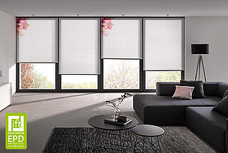 Modern eingerichtetes Wohnzimmer mit mehreren bodentiefen Fenstern, an denen weisse MHZ-DUETTE® Wabenplissees montiert sind.