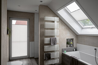 Plissees an Tür und Dachfenster in modernem Bad mit Wanne und schräger Decke.