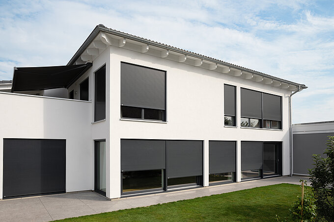 Modernes weisses Einfamilienhaus mit geschlossenen, aussenliegenden Metallbehängen Sonro an allen Fenstern.