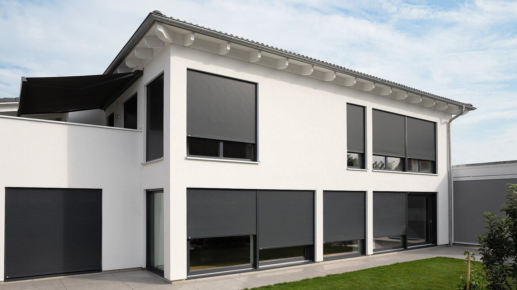 Modernes weisses Einfamilienhaus mit geschlossenen, aussenliegenden Metallbehängen Sonro an allen Fenstern.