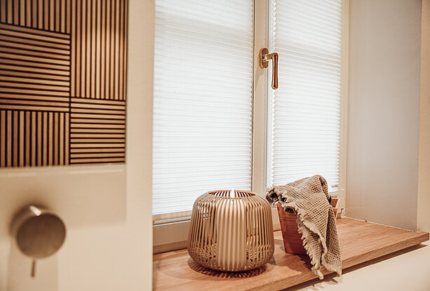 Weisses, halbtransparentes Plissee an einem modernen Fenster mit Holzfensterbank, dekoriert mit Schale und Stofftuch