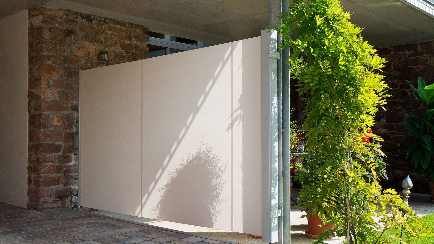 Seitenmarkise in hellbeige gespannt zwischen zwei Pfeilern als Sichtschutz unter einem Balkon.