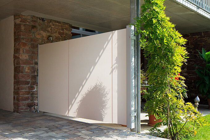 Seitenmarkise in hellbeige gespannt zwischen zwei Pfeilern als Sichtschutz unter einem Balkon.