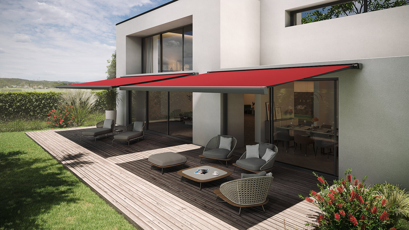 Zwei rote Gelenkarmmarkisen über Terrasse eines modernen Hauses mit Sitzgruppe auf Holzdeck.