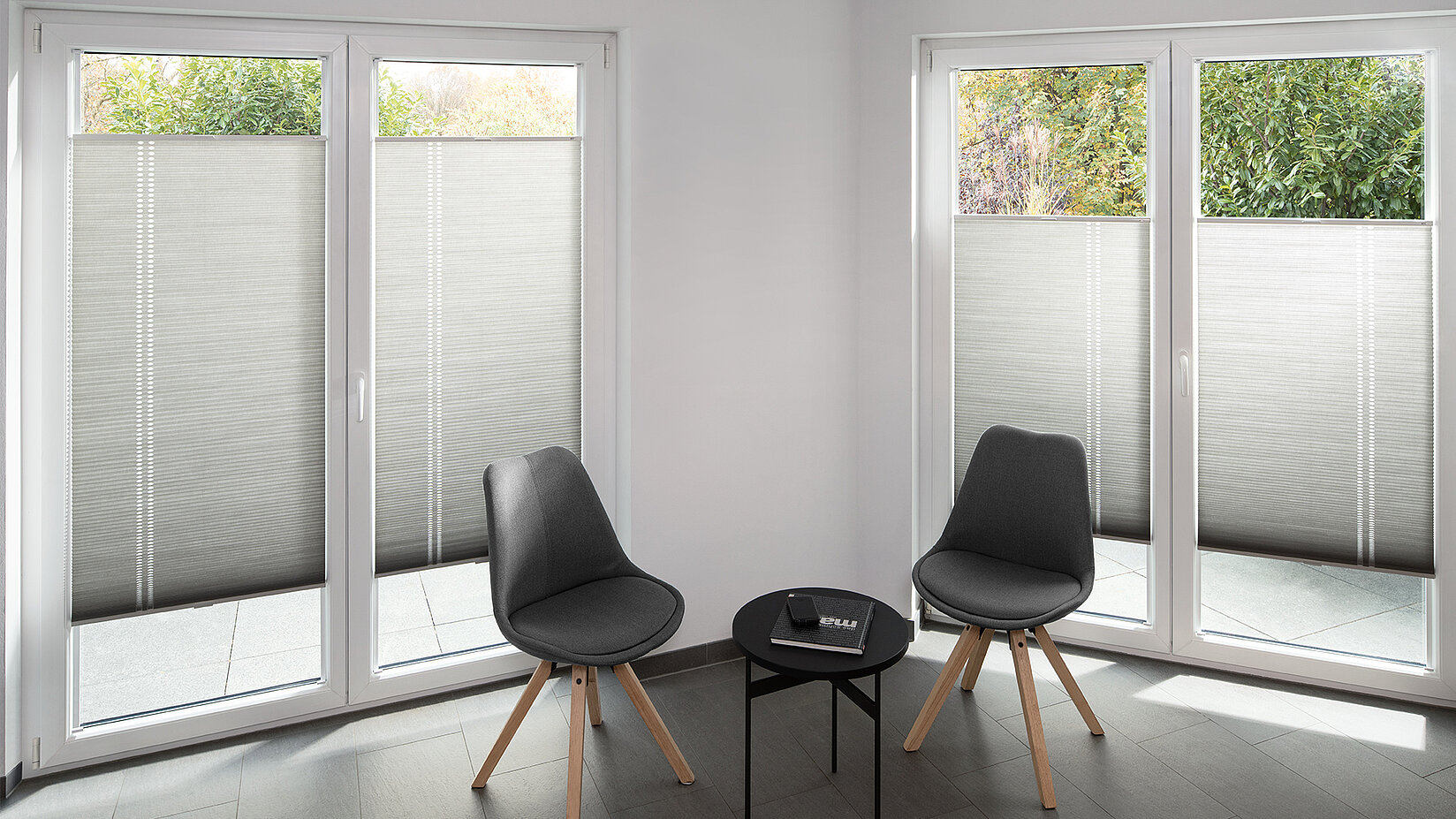 MHZ Wabenplissees im Design „Ellipsis“ an weissen Terrassenfenstern mit grauem Stoff und vertikalem Muster.