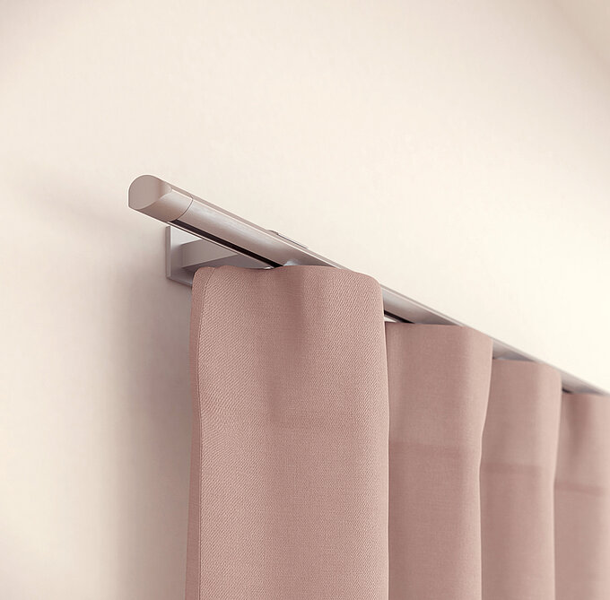 MHZ Vorhangstange „Kite“ in Aluminiumoptik, an der Wand montiert mit rosa Vorhängen.
