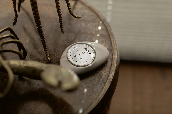 MHZ PowerView® Pebble-Fernbedienung zur Steuerung von Sonnenschutzprodukten, liegend auf einem Tisch.