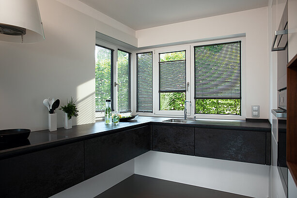 Küche mit mehreren Eckfenstern und innenliegenden Jalousien. Lamellen sorgen für Lichtregulierung und Sichtschutz.