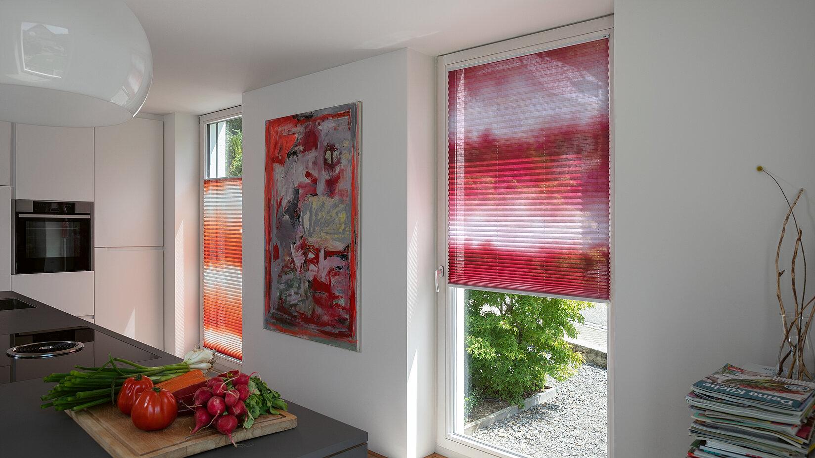 Plissee „Auarell“ mit rotem Aquarell-Motiv in moderner Küche mit viel Tageslicht.