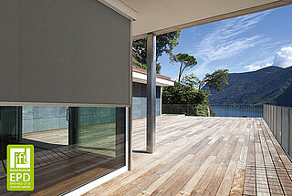 Eine überdachte Terrasse mit Holzbelag und Ausblick auf einen See. An der Fensterfront ist eine senkrechte MHZ-Markise als Sonnenschutz montiert.