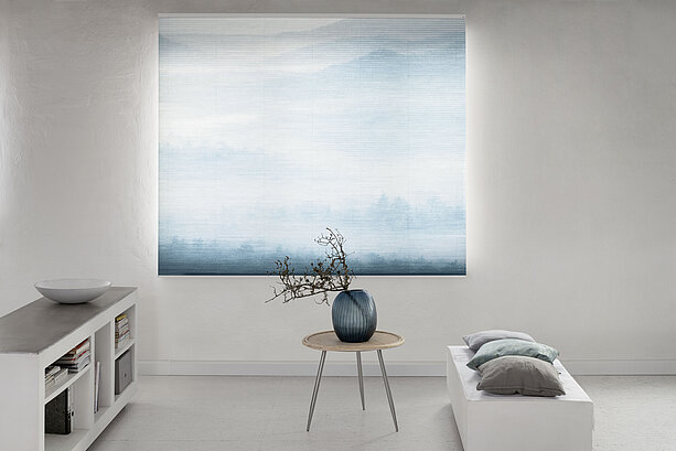 MHZ Wabenplissee mit sanftem Landschaftsmotiv in Blau, vor einem hellen Raum mit minimalistischer Einrichtung.