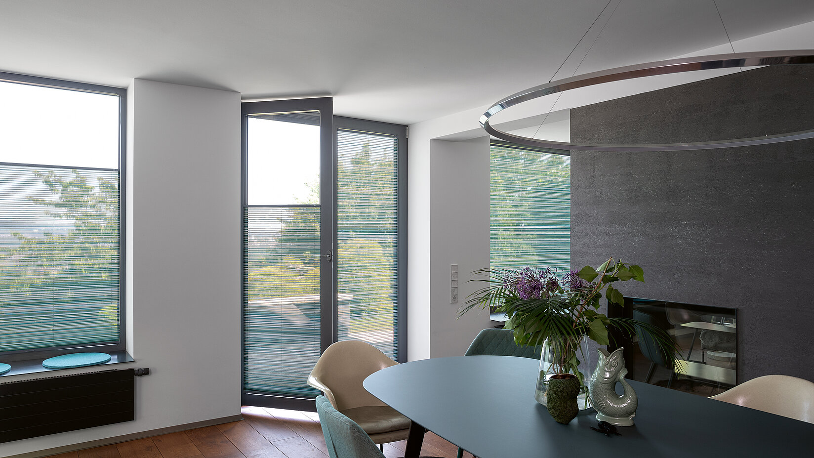 Petrolfarbene Plissees an bodentiefen Fenstern im modernen Esszimmer mit grünem Tisch.