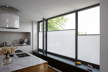 Weisse Plissees im unteren Fensterbereich in moderner Küche mit grossen Fensterflächen.