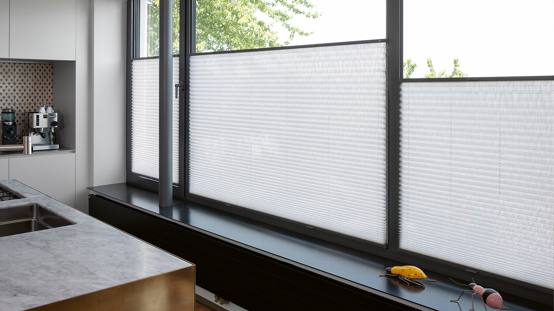 Weisse Plissees im unteren Fensterbereich in moderner Küche mit grossen Fensterflächen.