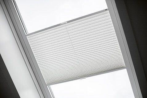 Weisses Plissee in einem Dachflächenfenster mit lichtdurchlässigem Stoff zur Lichtregulierung.