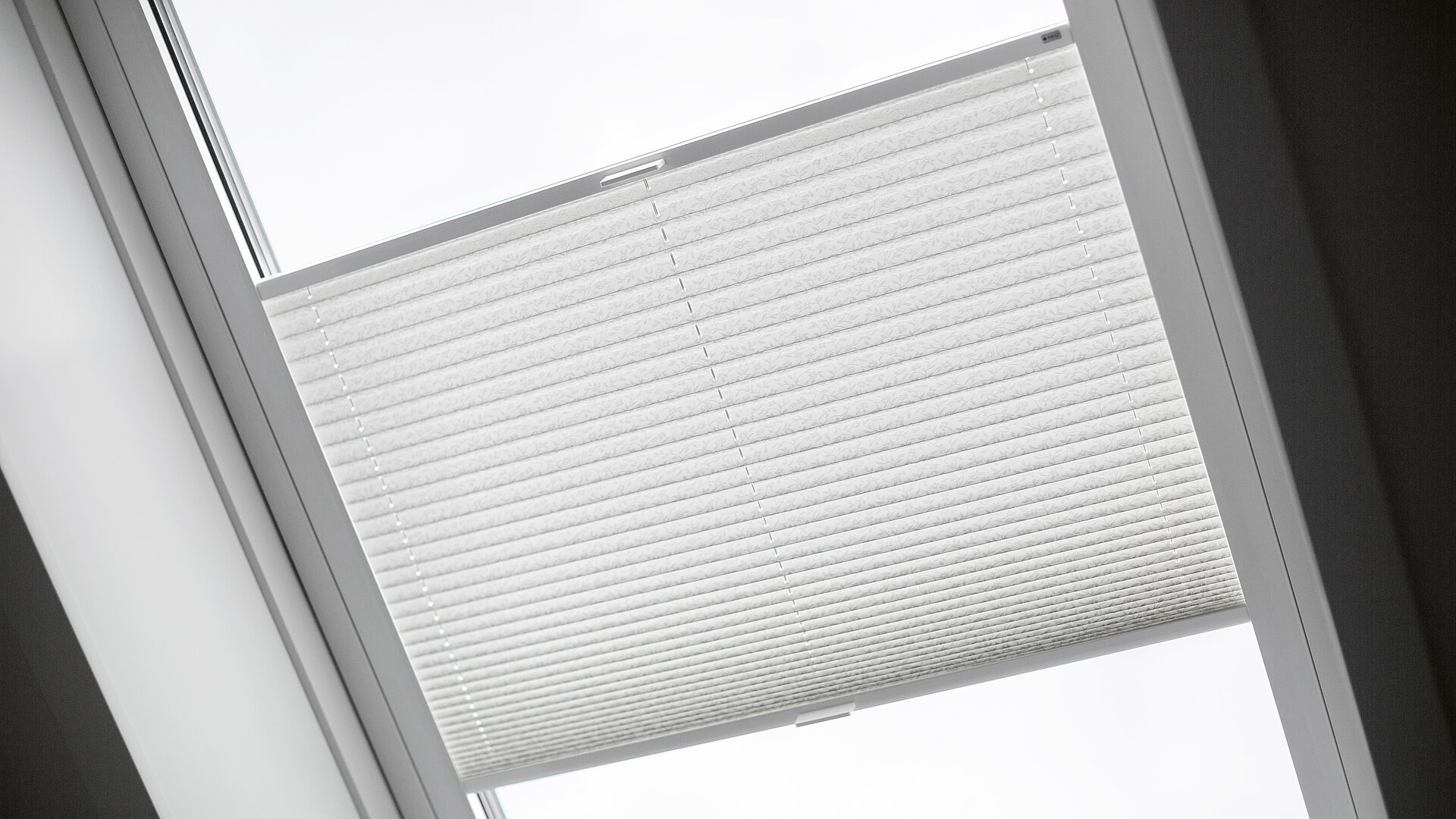 Weisses Plissee in einem Dachflächenfenster mit lichtdurchlässigem Stoff zur Lichtregulierung.