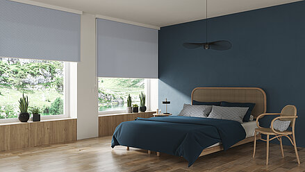 Modernes Schlafzimmer mit zwei grossen Fenstern und strukturierten, blauen Verdunkelungsrollos. Holzboden, Rattanbett und blaue Wand als Gestaltungselemente.