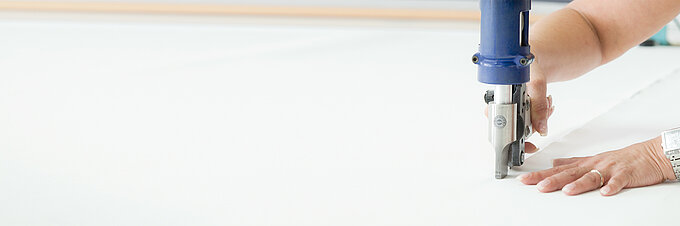 Nahaufnahme einer Hand beim präzisen Zuschnitt von Stoff mit einer Schneidemaschine.