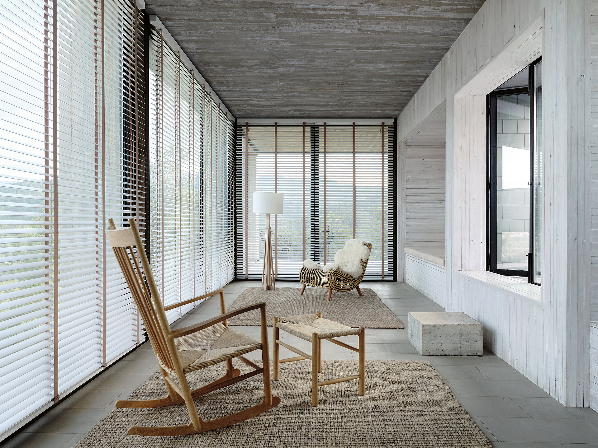 Heller Raum mit Holzjalousien, Schaukelstuhl und natürlicher Einrichtung im skandinavischen Stil.